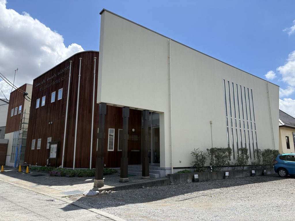 Modern two-tone building with a white wall and dark wood-clad section under a bright blue sky.