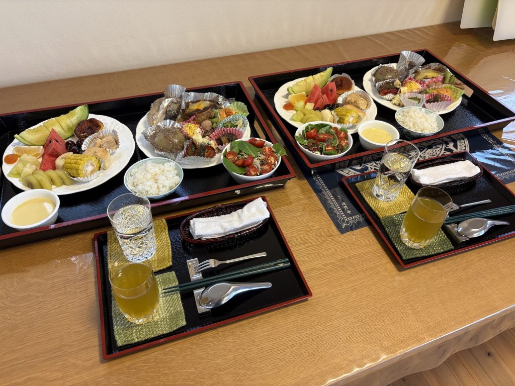Three black lacquered bento trays filled with fruit, rice, salads, and assorted bite-sized dishes and desserts on a wooden table