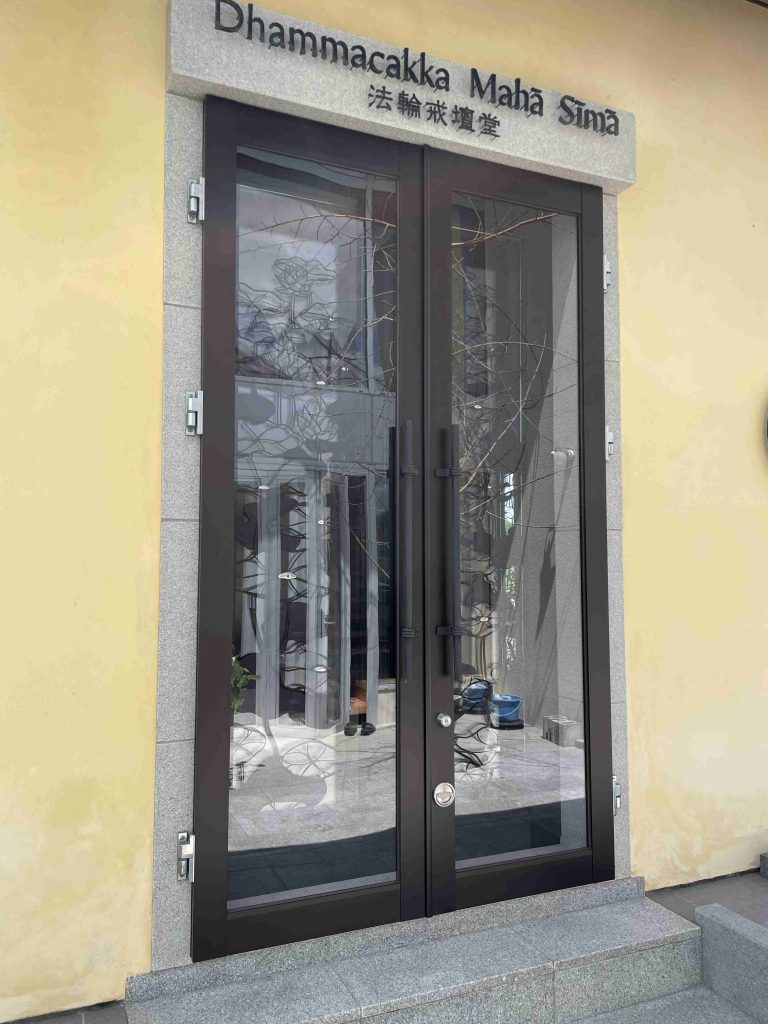 Double glass doors with dark frames set in a stone surround on a yellow exterior wall; building entrance visible.