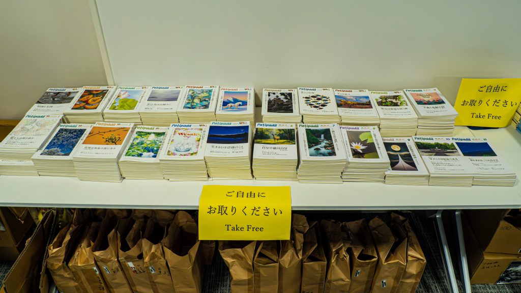 Stacks of Patipada magazines laid out on a table with bright yellow 'Take Free' signs in Japanese.