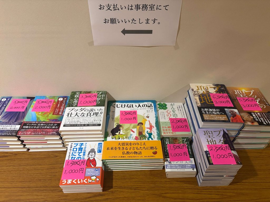 Shelf of Japanese books with pink price stickers in yen on the covers; sign above in Japanese indicating to proceed left.